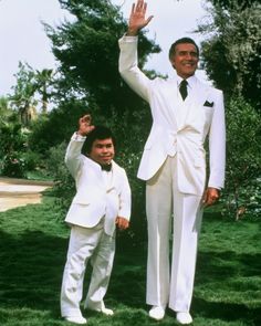 two men in white suits and ties standing next to each other with their hands up