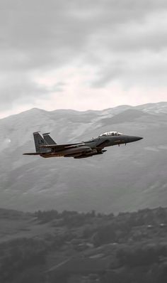 a fighter jet flying in the sky over mountains