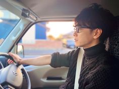 a woman sitting in the driver's seat of a car with her hand on the steering wheel