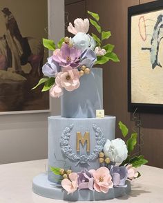 a three tiered blue cake with flowers on the top and initials on the side