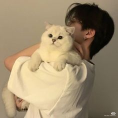 a woman holding a white cat in her arms while she is wearing a white shirt