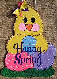 a wooden sign that says happy spring with a chick on it's head and an egg in the grass