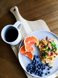 a plate with eggs, blueberries and oranges on it next to a cup of coffee