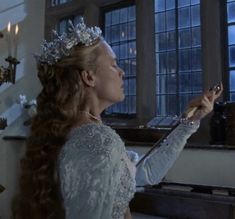 a woman wearing a tiara and holding a wand in her hand while looking out the window