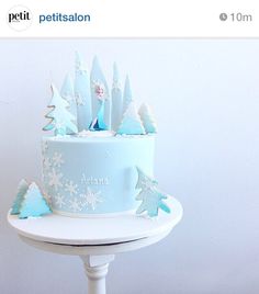 a white cake with blue frosting and snowflakes on it, sitting on top of a table