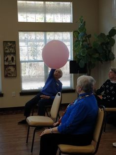 two elderly women sitting in chairs with balloons on their heads and one woman holding a pink balloon above her head