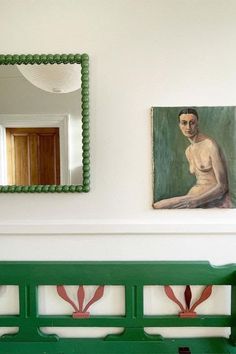 a green bench sitting in front of a painting on the wall next to a mirror