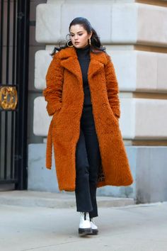 a woman in an orange coat is walking down the street