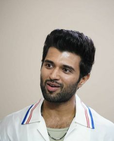 a man wearing a white shirt with blue and red stripes on the collar is looking at the camera