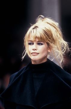 a woman with blonde hair walking down a runway wearing a black coat and matching heels