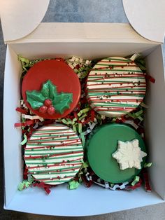 three decorated cookies in a box with holly decorations on the top and one cookie covered in icing