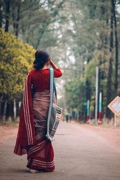 a woman is walking down the street with her hand on her head and wearing a red sari