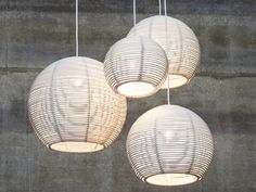 three white lanterns hanging from the ceiling in front of a concrete wall with no lights