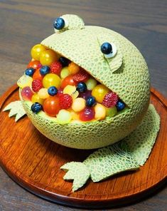 a frog made out of fruit sitting on top of a wooden plate