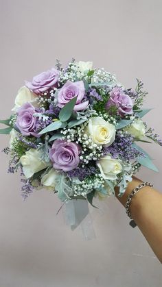 a bridal bouquet being held by a woman's hand with purple and white flowers