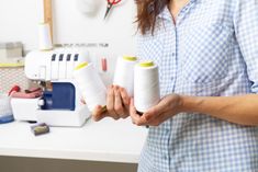 a woman is holding two spools of thread in her hands while standing next to a sewing machine