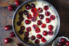 a cake with cherries and cream in a pan on top of a wooden table