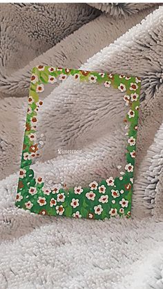 a green and white flowered frame sitting on top of a bed next to a blanket