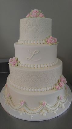 a three tiered wedding cake with pink flowers on it's side and the letter l on top