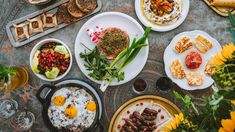 an overhead view of food and drinks on a table with breads, salads, eggs, and other foods