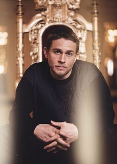 a man sitting in front of a golden chair with his hands on his knees and looking at the camera