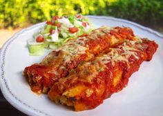 two enchiladas are sitting on a white plate next to a side salad