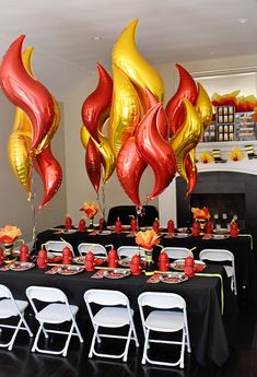 the table is decorated with red and gold balloons, black table cloths, and white chairs