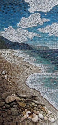 a mosaic tile wall hanging on the side of a building next to the ocean with rocks and pebbles