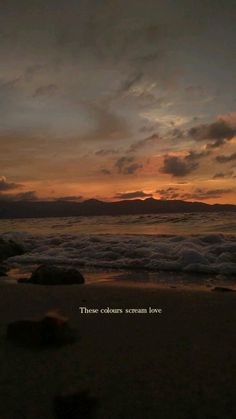 the sun is setting at the beach with waves coming in to shore and some rocks laying on the sand