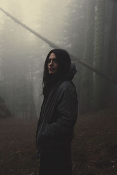 a woman standing in the woods on a foggy day