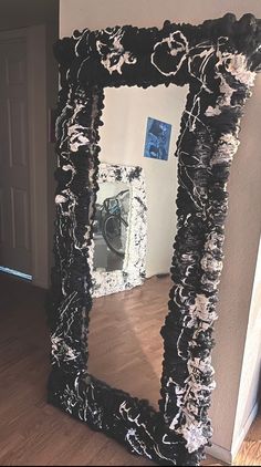 a black and white mirror sitting on top of a wooden floor next to a wall