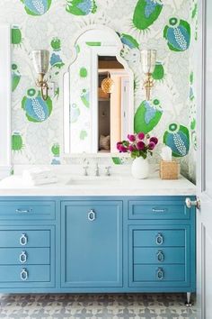 a bathroom with blue cabinets and green wallpaper on the walls, along with a large mirror