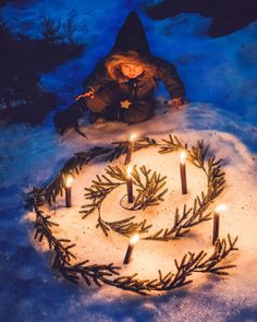 a person sitting in the snow next to a wreath with candles