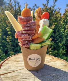 a cup filled with different types of food on top of a wooden table next to trees