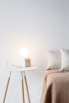 a small table with a lamp on it next to a bed