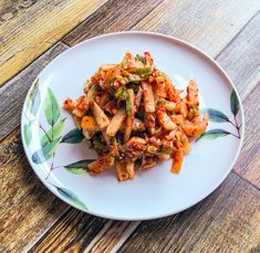 a white plate topped with pasta and sauce on top of a wooden table next to a fork