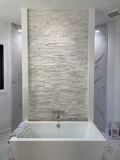 a large white bath tub sitting under a window next to a wall covered in marble