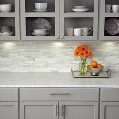 some orange flowers are in a vase on the kitchen counter top with plates and bowls