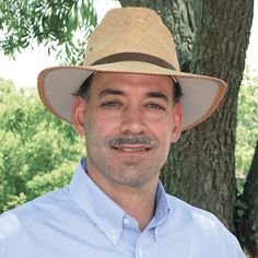 a man wearing a hat standing in front of a tree