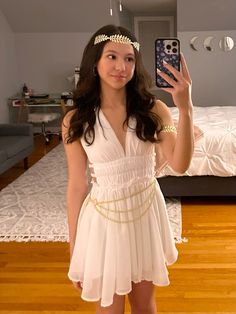 a woman taking a selfie in her bedroom wearing a white dress and headband