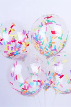 five clear balloons with sprinkles and colored confetti on the top