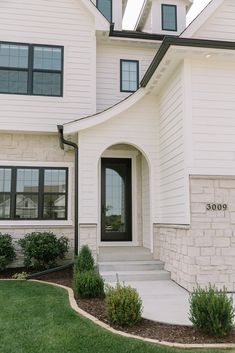 a white house with black trim and two story windows on the front door is shown