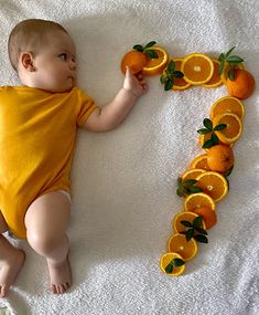 a baby laying on top of a bed next to oranges