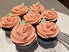 several cupcakes with pink frosting and green leaves on top are sitting on a white plate