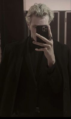 a man taking a selfie with his cell phone in front of him and wearing a black suit