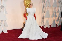 lady in white dress and red gloves standing next to an oscars statue on the red carpet