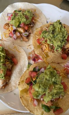 three tacos on a plate with guacamole and other food toppings