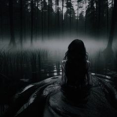 a woman sitting in the middle of a swampy area with fog coming from behind her