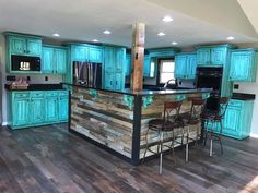 a large kitchen with blue cabinets and wooden flooring in the center is an island that has bar stools on it