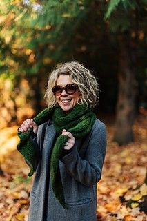 a woman standing in the woods wearing a green scarf and black leggings with her hands on her hips